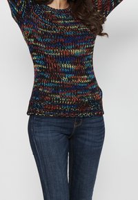 Meer gekleurde gebreide trui met een ronde hals en een getailleerd ontwerp, voorzien van een geribbelde zoom. Gecombineerd met donkerblauwe jeans, met een gestructureerd patroon.