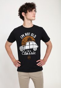 Černé bavlněné tričko s grafikou vintage auta a bílým a oranžovým textem. Design zahrnuje palm trees a pozadí se západem slunce.