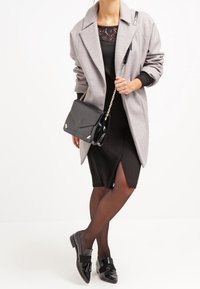 Gray oversized coat, black dress with lace detail, black handbag with gold accents, and glossy black shoes with bow detail.