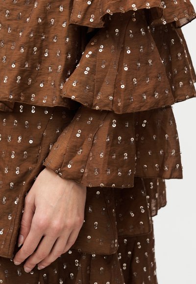 Robe marron à volants avec sequins ; présente des manches superposées, une texture douce, et un corsage ajusté qui met en valeur la main.