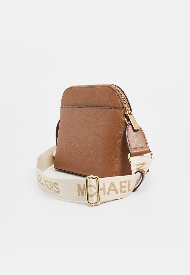 Sac à dos en cuir synthétique marron avec un dessus arrondi, des accents en métal doré et une large sangle arborant le nom de la marque en beige.