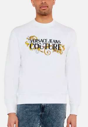 Sweatshirt blanc arborant le logo "Versace Jeans Couture" en noir avec des accents décoratifs dorés et blancs, et un col côtelé.