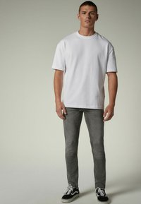 Valge lühikeste varrukatega T-särk, hall slim-fit teksapüksid ja mustad valged spordijalatsid. Lihtne disain klassikalise ümmarguse kaeluse ja tavalise pikkusega.
