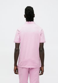 Rožinė polo marškinėliai su minkšta tekstūra, trumpomis rankovėmis ir klasikiniu apykakle, parodyta iš nugaros, derinama su atitinkančiomis kelnėmis.