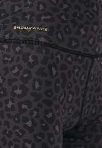 Mustat legginsit, joissa on teksturoitu leopardinprinttimalli, kultainen "ENDURANCE" -logo ja kontrastiväriset mustat ompeluyksityiskohdat.