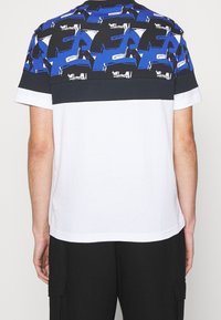 Tričko s krátkým rukávem s modro-černým abstraktním vzorem a bílými akcenty. Bavlněný materiál s pevným bílým spodním dílem a tmavými rukávy.