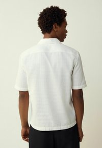 Short-sleeve, white shirt featuring a textured pattern, relaxed fit, and a standard collar. The back shows a yoke design and rounded hem.