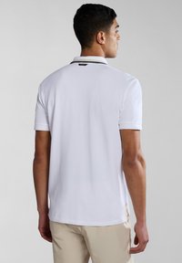 Polo bianco a maniche corte, colletto a contrasto, realizzato in tessuto liscio. Design minimalista con spacchi laterali all'orlo.
