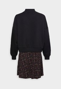 Pulóver negro de manga larga con puños y cuello acanalados, combinado con una minifalda negra que presenta un pequeño patrón floral multicolor.