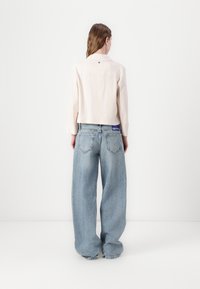 Svetlo roza skrajšan jopič z dolgimi rokavi, v kombinaciji z oversized svetlo modrimi denimsko hlačami, ki imajo zadnje žepke in vijolično etiketo.