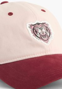 Căciulă cu un coronita din bumbac roz deschis și o vizieră din suede burgund. Prezintă un patch detaliat cu un grafic de urs pe partea din față.