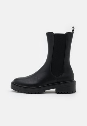 Svart ankelboot gjord av glatt läder med elastiska sidopaneler, rund tå och kraftig gummisula. Utrustad med en ögla för enkel påtagning.
