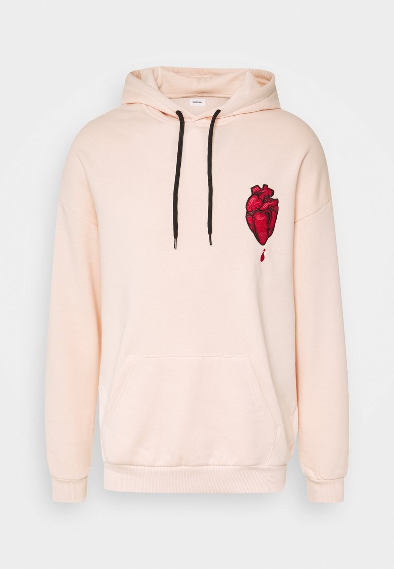 Sudadera de color rosa claro con cordones negros, bolsillo frontal y gráfico de un corazón anatómico rojo con una gota de sangre en el pecho.