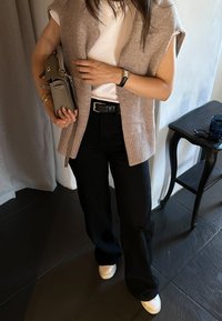 Ljusbrun stickad väst över en vit skjorta, svarta höga byxor och vita sneakers. Tillbehören inkluderar en grå handväska och klocka.