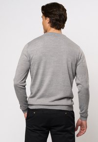 Grijze gebreide trui met lange mouwen, ronde hals en geribbelde manchetten. Gecombineerd met zwarte broek. Zachte textuur en eenvoudig, klassiek ontwerp.