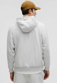 Grå hættebluse lavet af blødt stof, med en kængurulomme og ribbede manchetter. Bæres med en beige kasket, der viser et enkelt design.