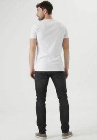 Camiseta blanca de manga corta combinada con unos vaqueros oscuros ajustados. Los vaqueros tienen un estilo clásico y detalles sutiles, rematados con calzado casual.