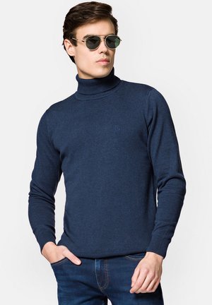 Granatowy sweter z golfem, wykonany z miękkiego, dzianinowego materiału; posiada długie rękawy oraz subtelne logo na piersi; połączony z okrągłymi okularami przeciwsłonecznymi.