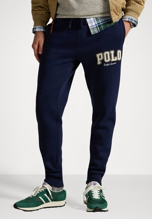 Marineblauwe joggingbroek met een trekkoord in de tailleband en geborduurd "Polo" logo. Gecombineerd met groene sneakers met witte strepen en gestructureerde accenten.
