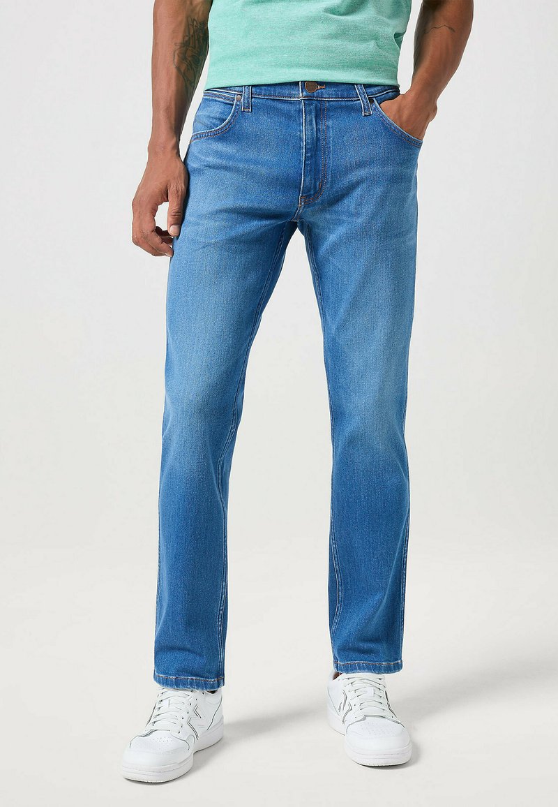 Jeans in denim blu chiaro con taglio dritto, cinque tasche e cuciture a contrasto, abbinati a sneakers bianche.