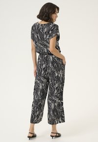 Black and white marbled jumpsuit with short sleeves, elastic waistband, and wide-leg design. Smooth fabric with subtle sheen and side pockets.