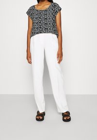 Haut court à motif noir et blanc avec un col rond, associé à un pantalon blanc taille haute et des sandales noires. Tissu lisse et coupe décontractée.