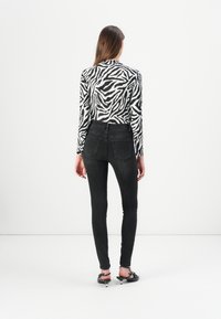 Pantalones vaqueros ajustados negros combinados con una blusa de manga larga de estampado de cebra en blanco y negro. La blusa presenta un diseño entallado y una textura suave.