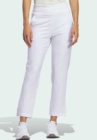 Vita idrottsbyxor med hög midja, sidofickor, rak ben-design och delade nederkanter, i kombination med vita träningsskor.