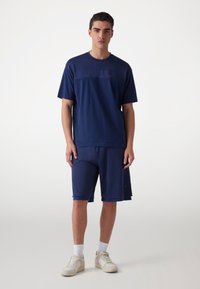 Námořnický sportovní outfit skládající se z krátkého rukávu síťového topu a odpovídajících šortek, oboje vyrobené z prodyšných materiálů, doplněný lehkými teniskami.