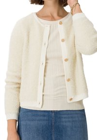 Weißer, flauschiger Cardigan mit rundem Ausschnitt, strukturiertem Stoff, gerippten Bündchen und sechs goldfarbenen Knöpfen auf der Vorderseite. Über einem hellen Oberteil getragen.