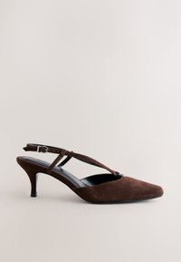 Chaussure à talon kitten en daim marron, avec bout pointu et bride à boucle sur fond neutre.