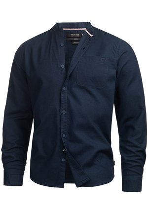 Chemise en lin navy avec col montant, manches longues et boutons sur le devant. Dispose d'une poche poitrine et d'une texture subtile sur l'ensemble.