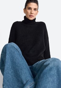 Fekete bordázott garbós pulóver könnyű kék, oversized farmernadrággal párosítva. Puha textúra és laza fazon.