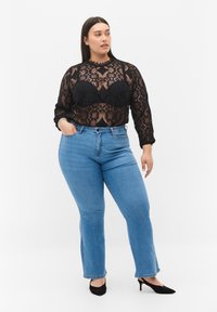 Top negro de encaje de manga larga con patrones florales y escote de pico, combinado con jeans de cintura alta en azul claro y tacones negros.
