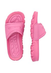 Vaaleanpunaiset kumisaappaat, joissa on leveä hihna, teksturoitu pohja ja tukevat pohjat. Hihnassa ja sivuissa on kohotettu logo.