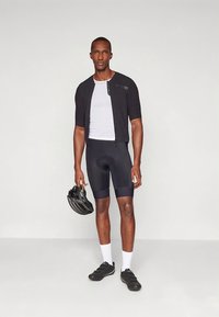 Figursydd svart cykeltröja med korta ärmar, vit meshundertröja och svarta cykelshorts. Tillbehör inkluderar svart hjälm och skor.