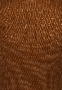 Bruine gebreide stof met een gestructureerd, verhoogd patroon; heeft een warme tint en een constante weving door het materiaal.