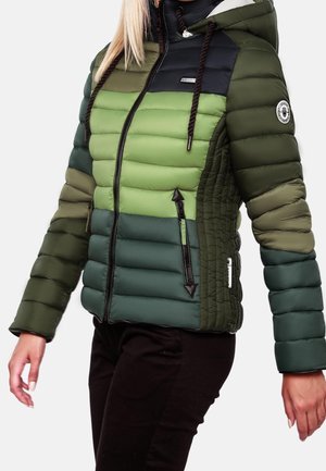 Femme portant une doudoune verte color-block avec une fermeture éclair noire et une capuche, associée à un pantalon noir.