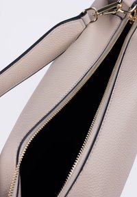 Borsa a mano in pelle beige con finitura testurizzata, dotata di una cerniera dorata e dettagli neri. L'interno è scuro e spazioso.