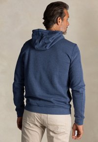 Donkerblauwe hoodie van zacht materiaal, met een trekkoordcapuchon, ribgebreide manchetten en een semi-gestructureerd ontwerp. Gekocht met lichtgekleurde broek.