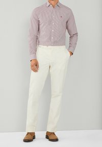 Chemise à rayures rouges et blanches avec col boutonné, associée à un pantalon crème et des chaussures en daim marron. Design simple et ajusté.
