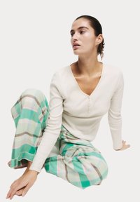 Lichtcrème katoenen top met lange mouwen en knoopdetails; groene en pastelgetailleerde pyjamabroek met wijde pijpen en een zachte textuur.
