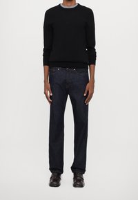 Maglione nero lavorato a maglia con scollo rotondo, abbinato a jeans dritti di colore blu scuro. Completa il look un paio di scarpe di pelle marrone.