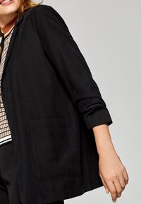 Svart blazer i ett slitstarkt tyg med slagkrage, långa ärmar och en framficka. Skräddarsydd passform och minimalistisk design.