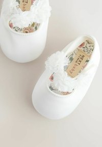 Valged satiinist beebijalatsid lillelisede aktsentidega, ümarad varbad ja dekoratiivne pitsäär. Lillemuster sisetald lisab detaili.