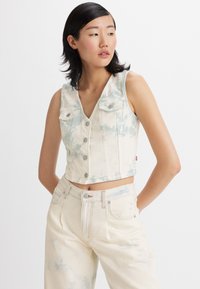 Cropped denim vest in cream with light blue tie-dye patterns. Features a V-neck, button closure, and two chest pockets. Smooth texture.