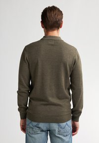Maglione a maglia verde oliva con maniche lunghe e colletto, dotato di polsini e orlo a coste. Indossato con jeans blu chiaro, vista posteriore.