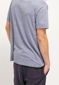 Šedé tričko s krátkým rukávem a volným střihem, viděné ze zadní strany. Design obsahuje kulatý výstřih.