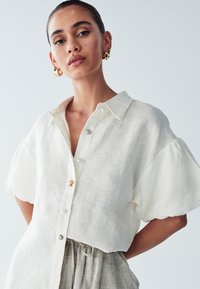 Witte linnen overhemd met korte mouwen, een klassieke kraag, een knoopsluiting aan de voorkant en een decoratieve steraccent nabij de bovenste knoop.