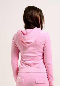 Felpa in pile rosa con cappuccio attaccato, vestibilità slim, maniche lunghe e tessuto testurizzato. Presenta una cintura e una leggera elasticità.
